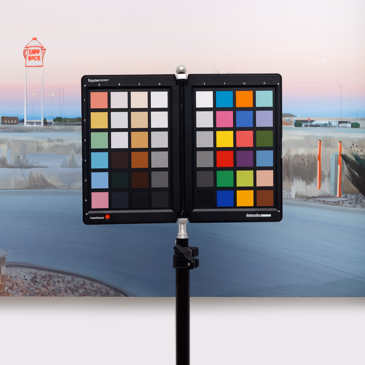 Color calibration chart on a stand in front of a landscape painting, set up before photographing the work
