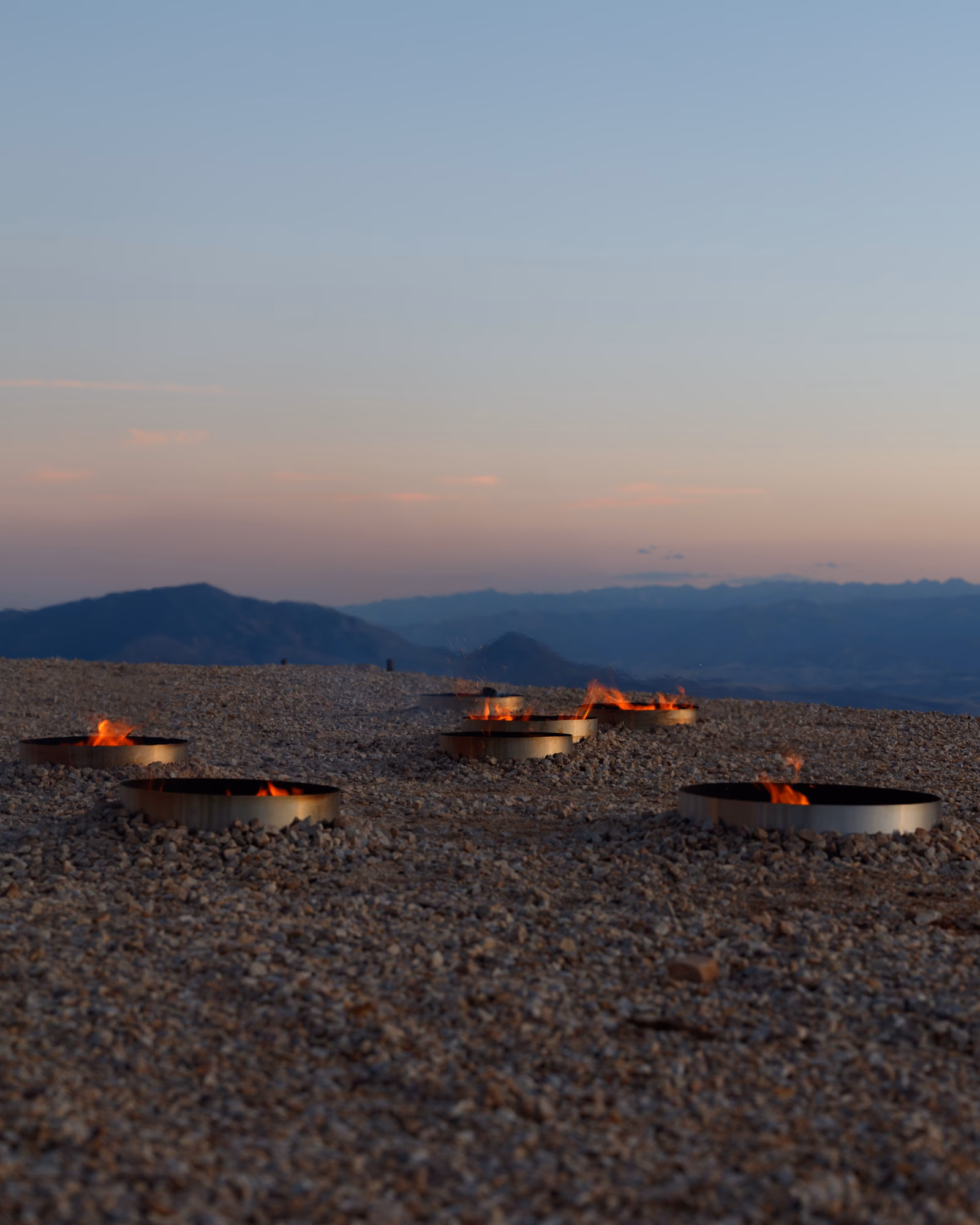 Outdoor fire bowl installation on desert landscape at dusk with mountain backdrop
